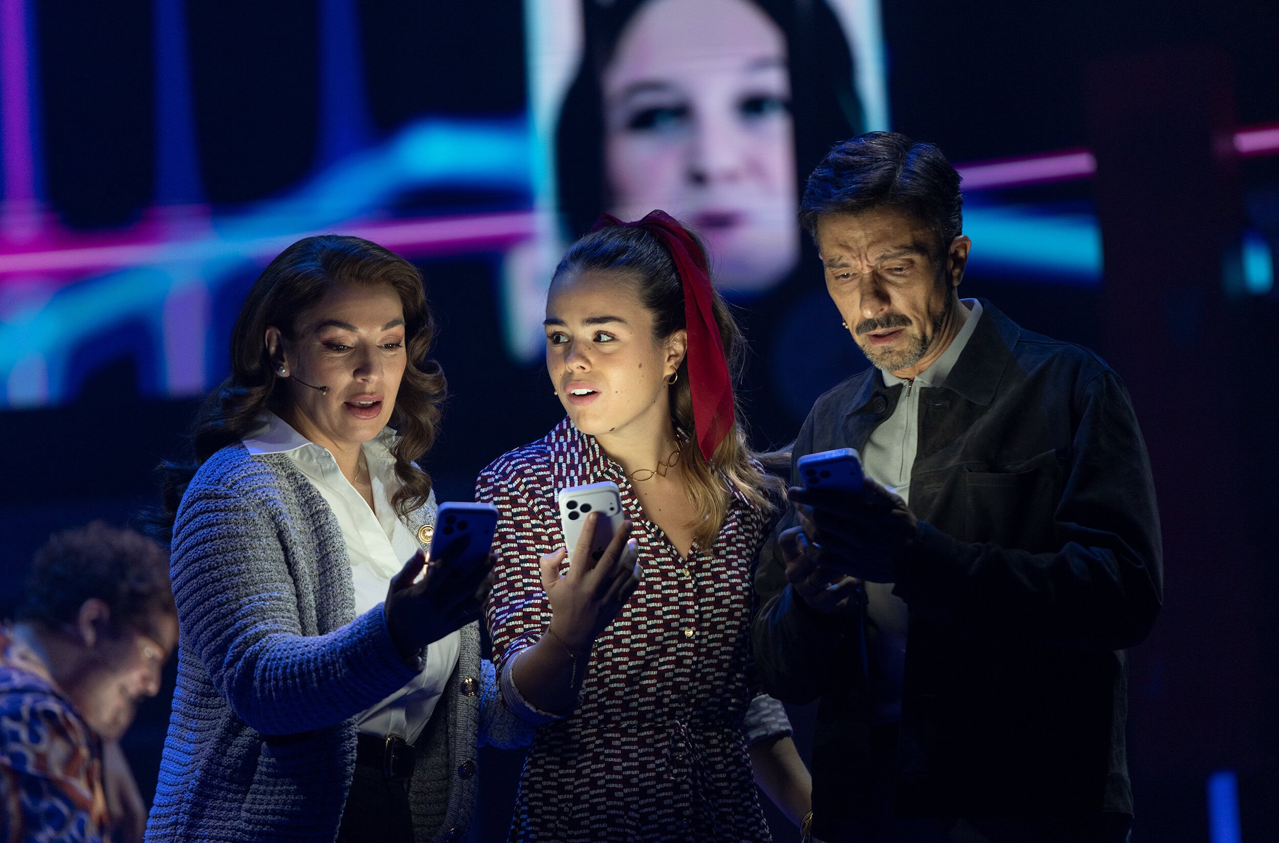 La familia Murphy observa mensajes en sus teléfonos ante proyecciones de redes sociales.